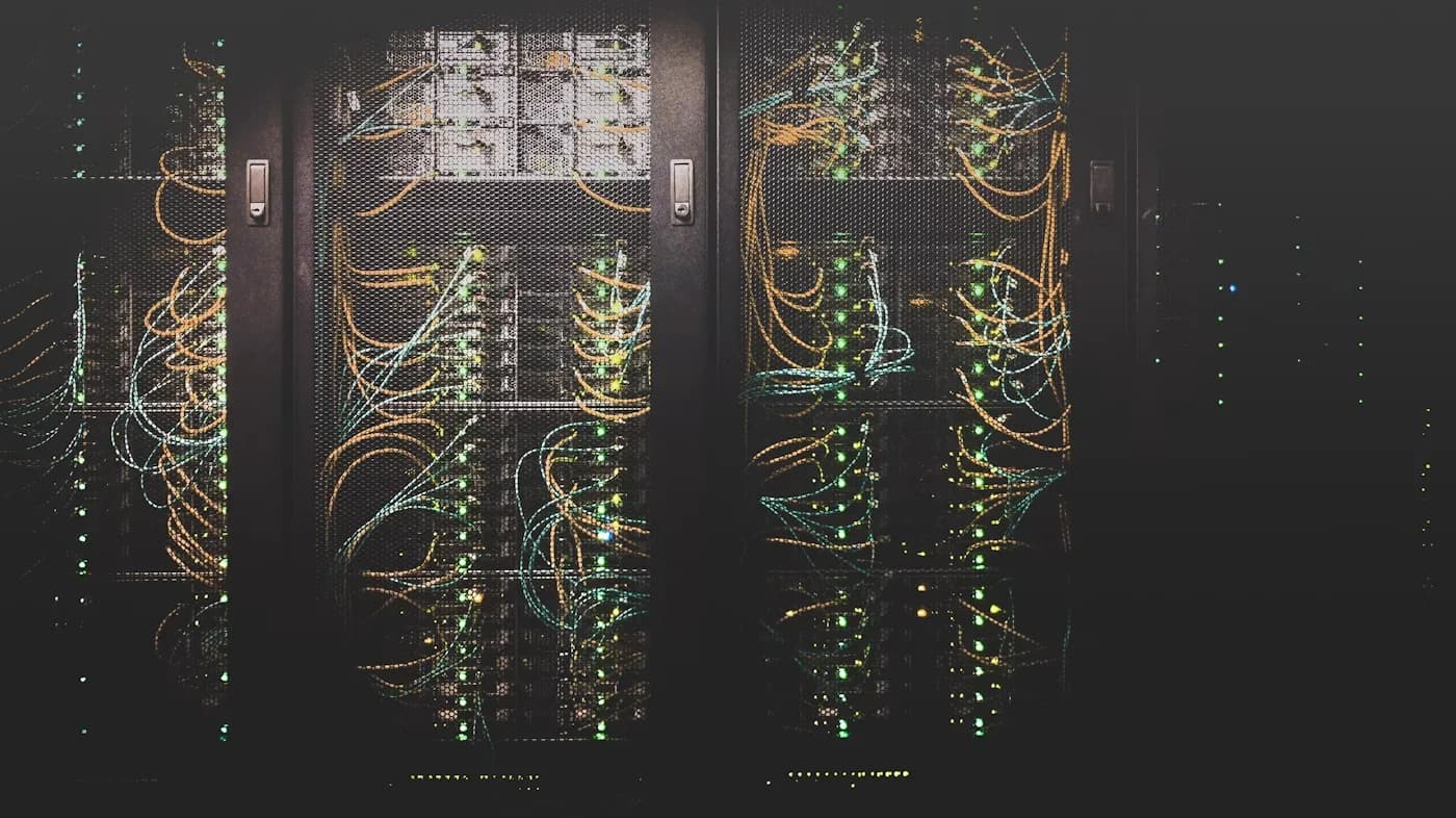 Dark equipment cabinets in a dim comms room with mesh doors open and patch leads looped between shelves.